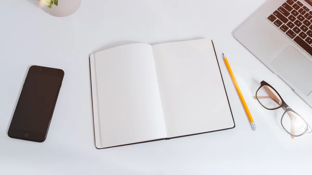 Mesa de trabajo con libreta abierta, portátil, móvil y lápiz para planificar contenido SEO a partir de noticias del sector.