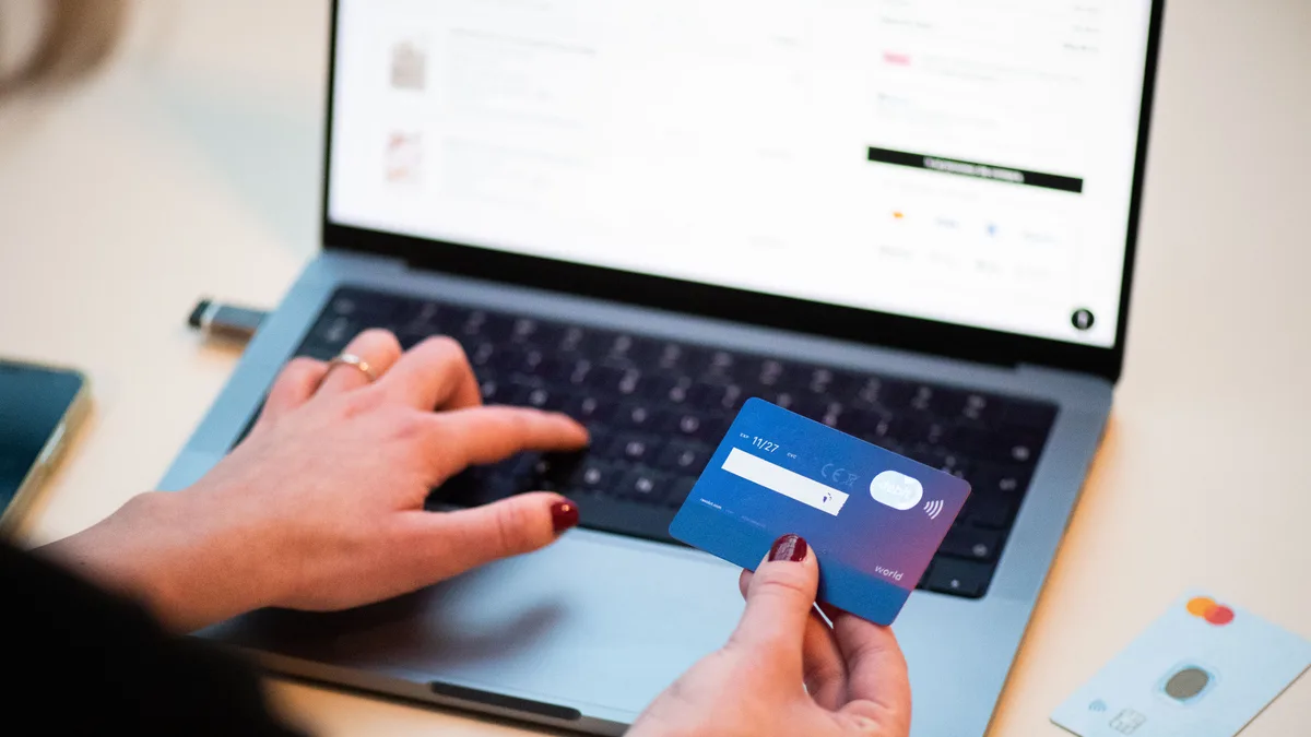 Persona comprando online con tarjeta bancaria frente a un portátil, como contexto para elegir entre marketplace y tienda propia.